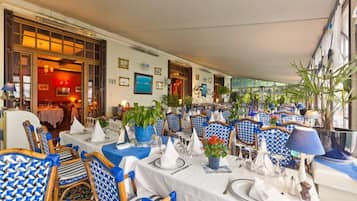 A restaurant with tables set for dining, blue patterned chairs, and potted plants.