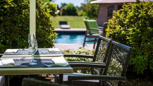 A dining table set outdoors with a view of a swimming pool and greenery. - l'Abreuvoir (Heric)