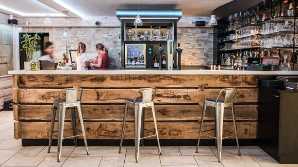 A bar area with a wooden counter, metal stools, and a variety of glassware and bottles. - l'Abreuvoir (Heric)