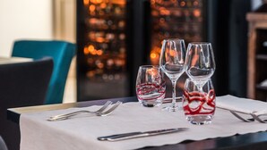 A dining table set with wine glasses and cutlery, with a cityscape view through a glass wall. - l'Abreuvoir (Heric)