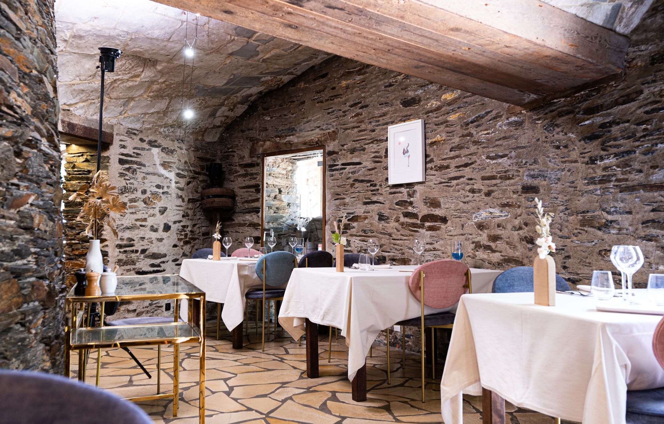 Un comedor rústico con paredes de piedra, vigas de madera y mesas dispuestas para comer.