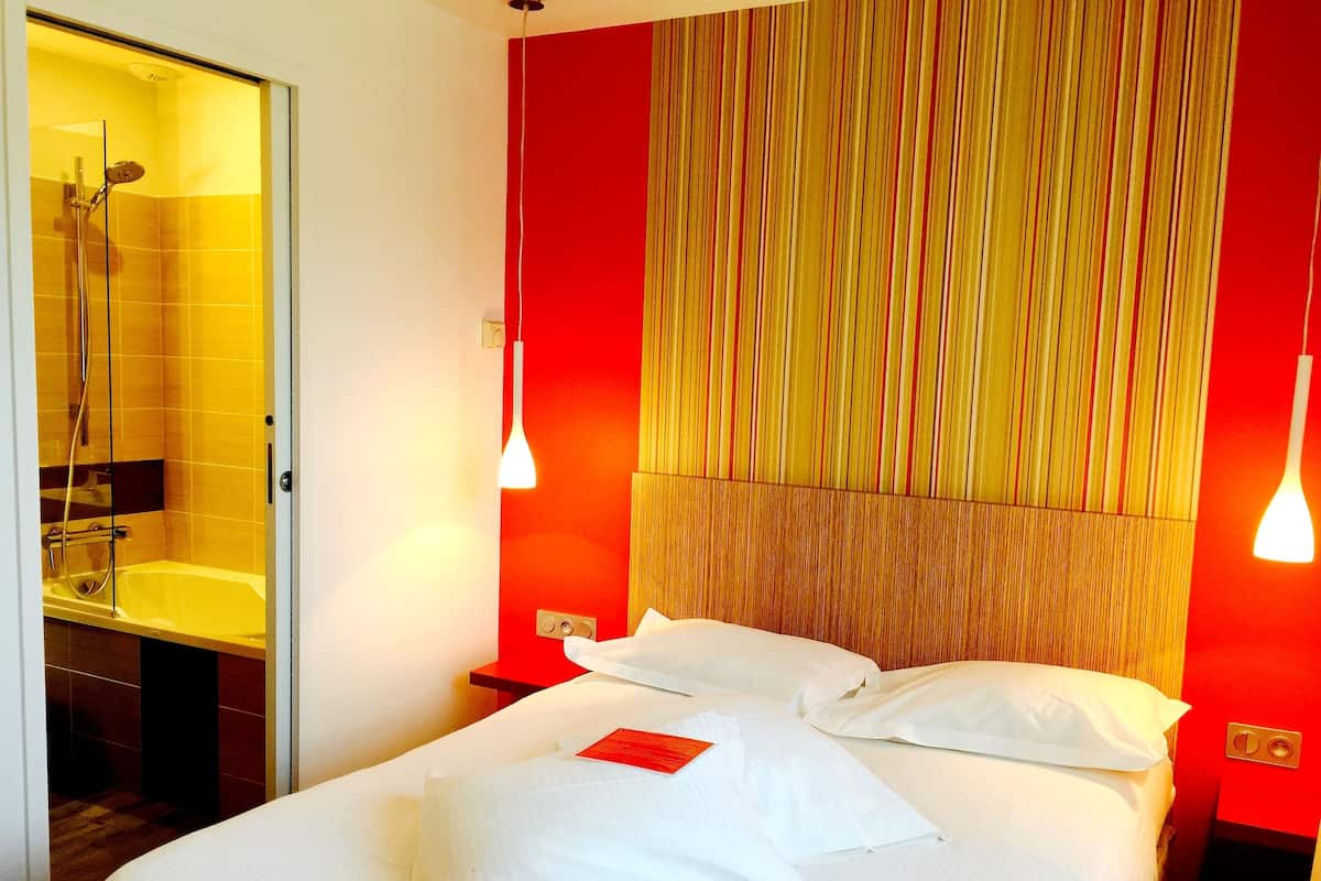 Habitación de hotel con cama, mesita de noche, pared decorativa roja y zona de ducha.