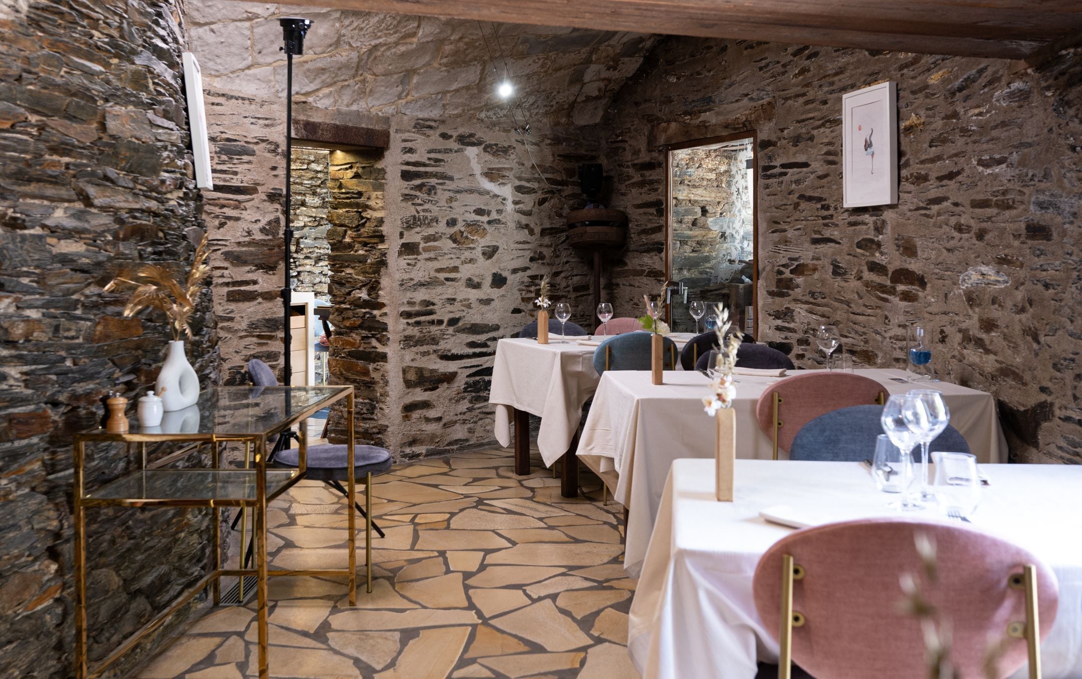 Un coin repas rustique avec des murs en pierre, des tables dressées et un mélange de chaises modernes et classiques.