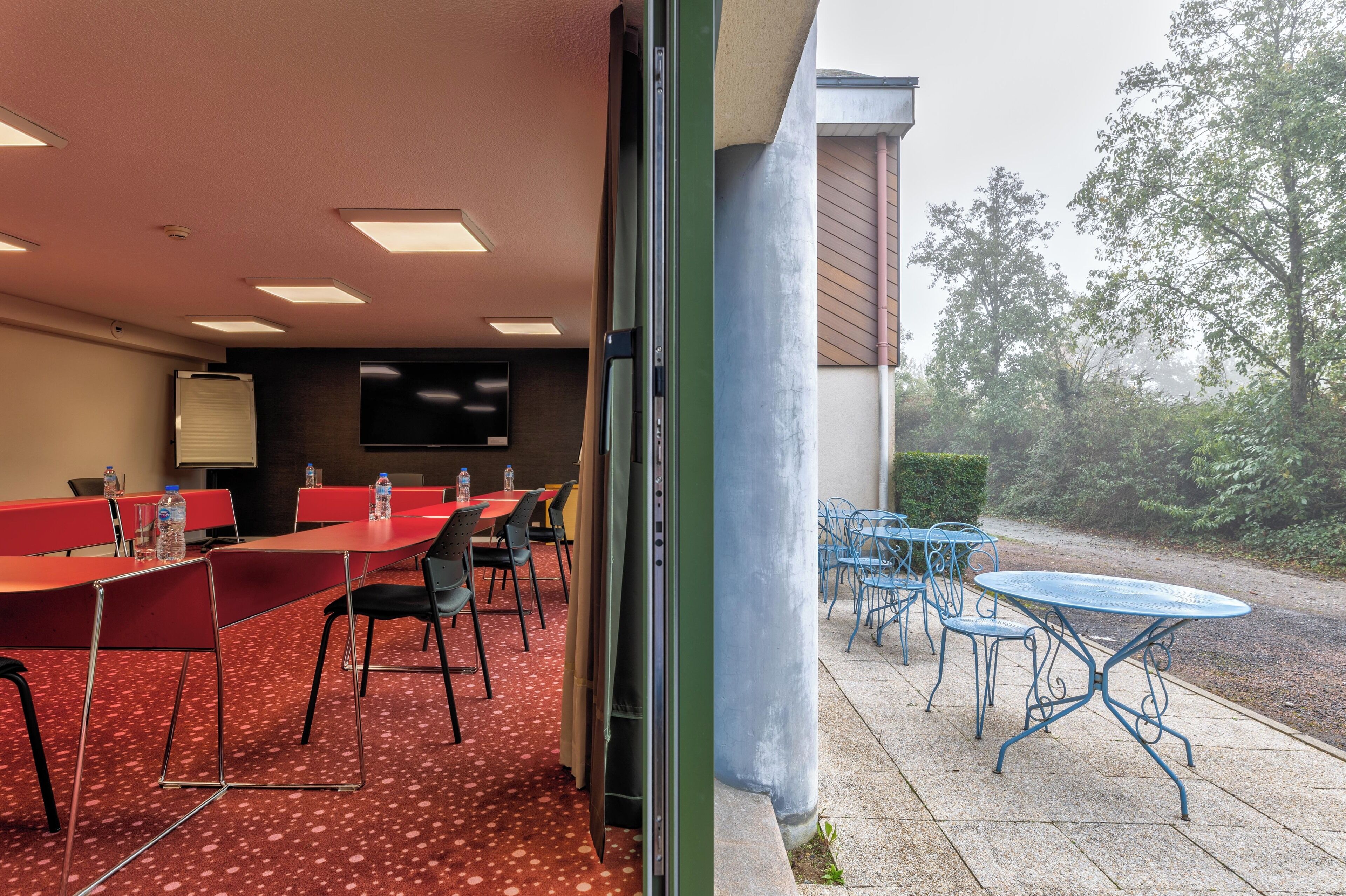 Une salle de conférence avec des tables et des chaises rouges, un écran de projection et un distributeur d’eau.
