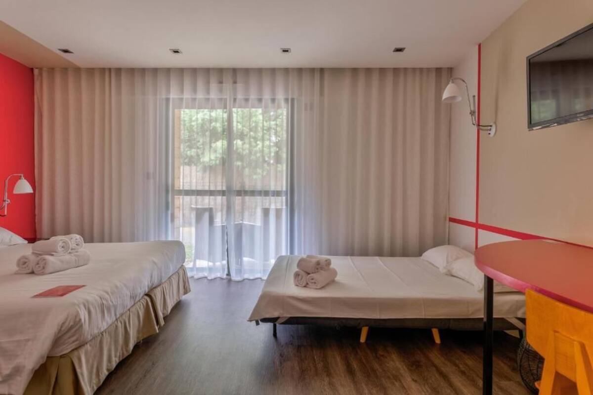 Habitación de hotel con dos camas, una mesa y un ventanal con cortinas.
