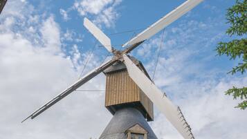 A traditional windmill with wooden sails and a conical base, set against a partly cloudy sky.