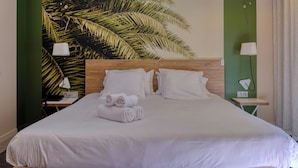 Ett hotellrum med en stor säng, gröna väggar och en väggmålning med tropiska blad.