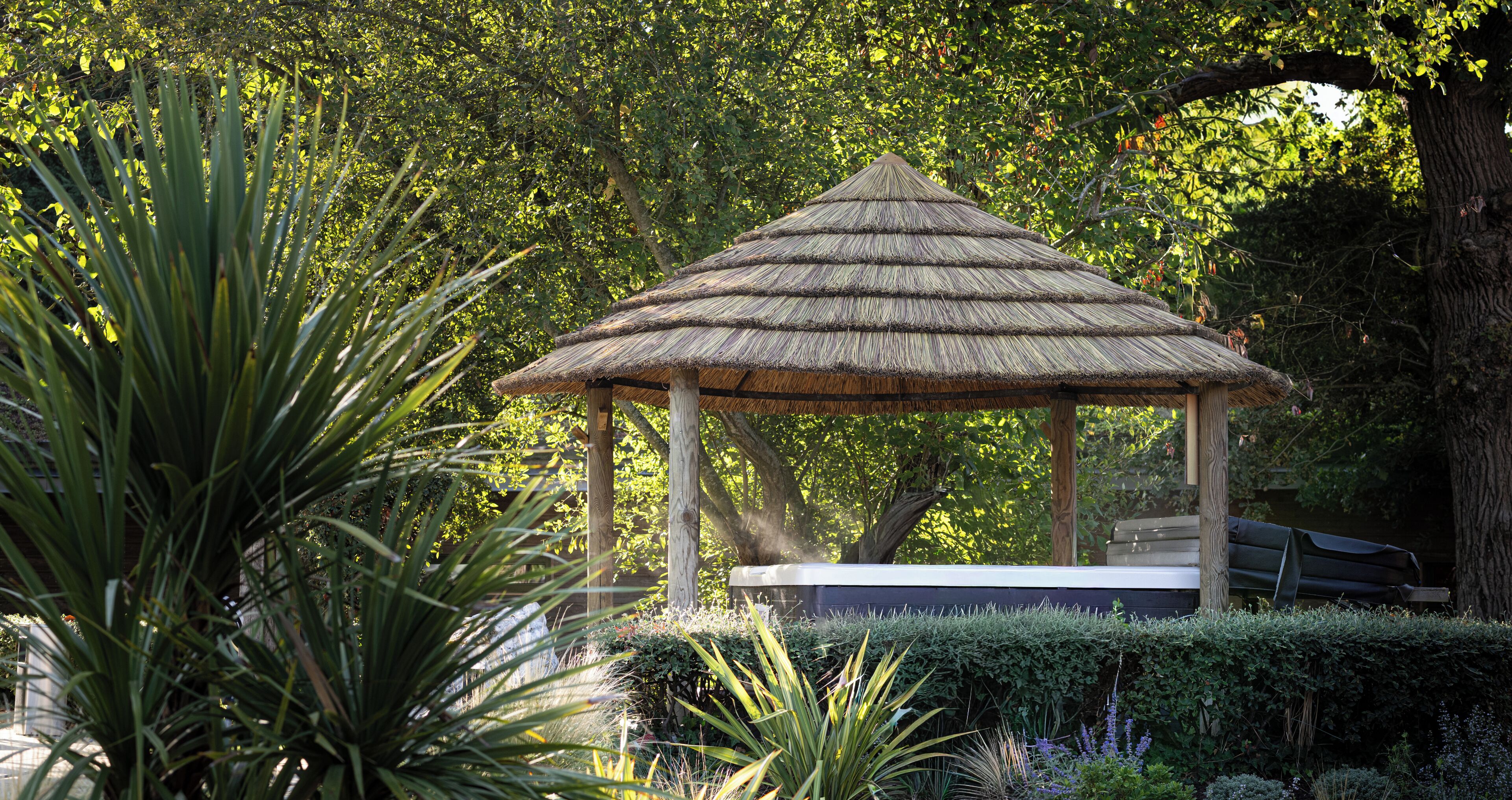 A gazebo with a thatched roof, surrounded by lush greenery and trees.