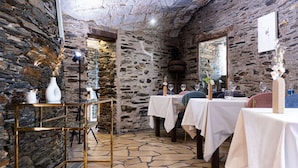 Ein rustikales Interieur mit Steinwänden, gedeckten Tischen und einem goldrahmenartigen Regal mit Dekorationsobjekten.