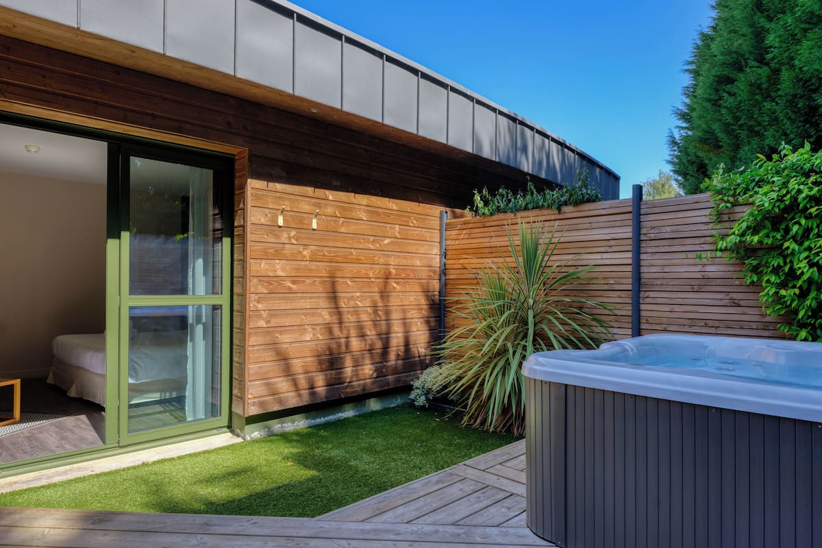 Una casa moderna con un ventanal que da a un dormitorio, una terraza de madera y un jacuzzi.