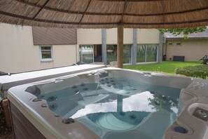 A hot tub with a thatched roof overhead, surrounded by a well-maintained lawn and a house in the background. - Logis Hôtel Domaine du Moulin Cavier - Restaurants & Spa (Avrille)