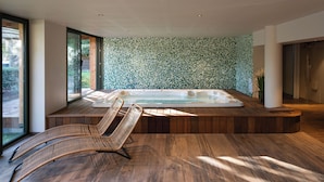 Ein moderner Wellnessraum mit Holzboden, einer großen Whirlwanne und einem Korbsessel.