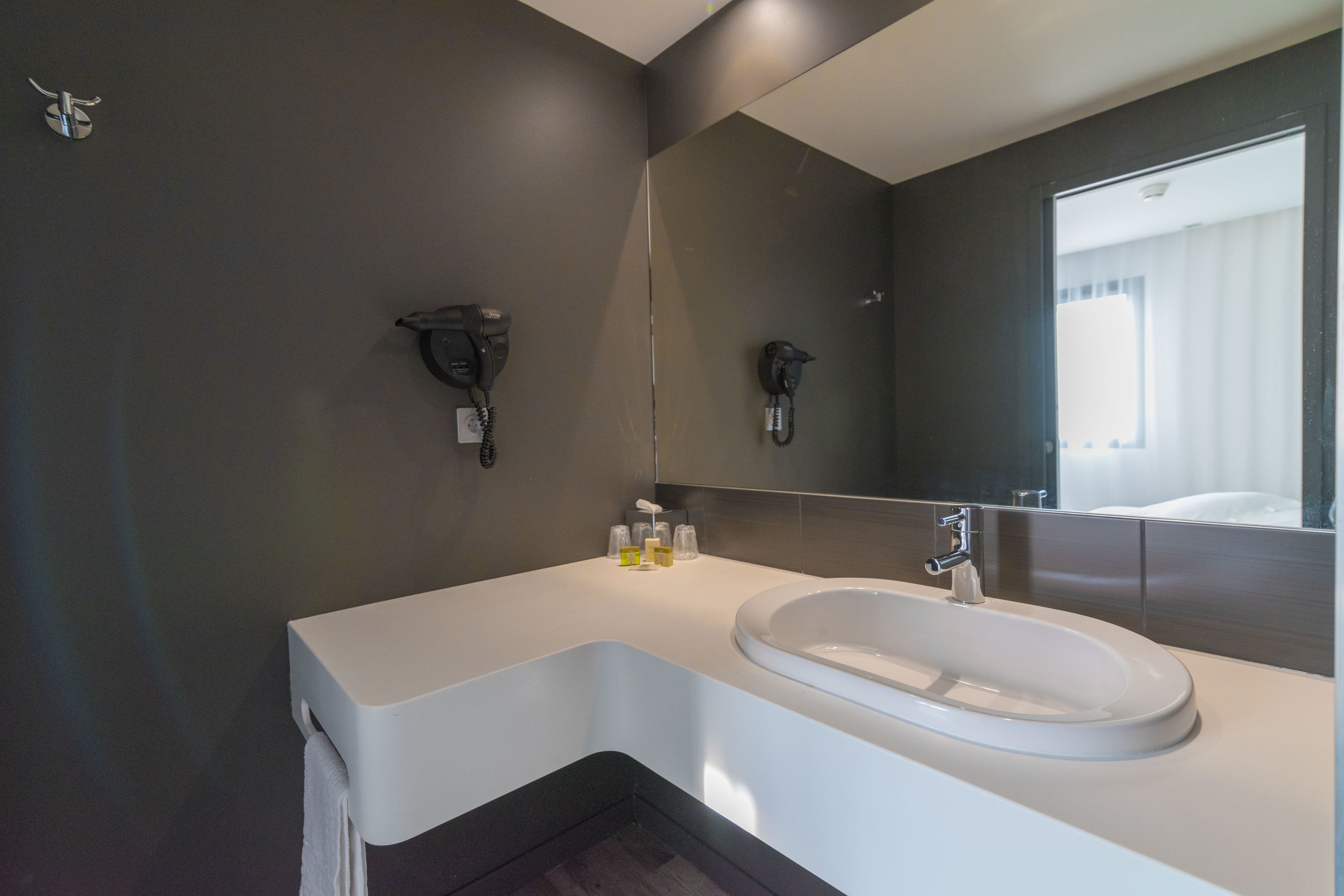 Une salle de bain moderne avec un lavabo blanc, des murs sombres et un grand miroir.
