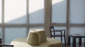 Un espace de détente moderne, avec un canapé incurvé, un fauteuil en bois et une petite table. De grandes fenêtres laissent entrer la lumière naturelle et illuminent l’espace.