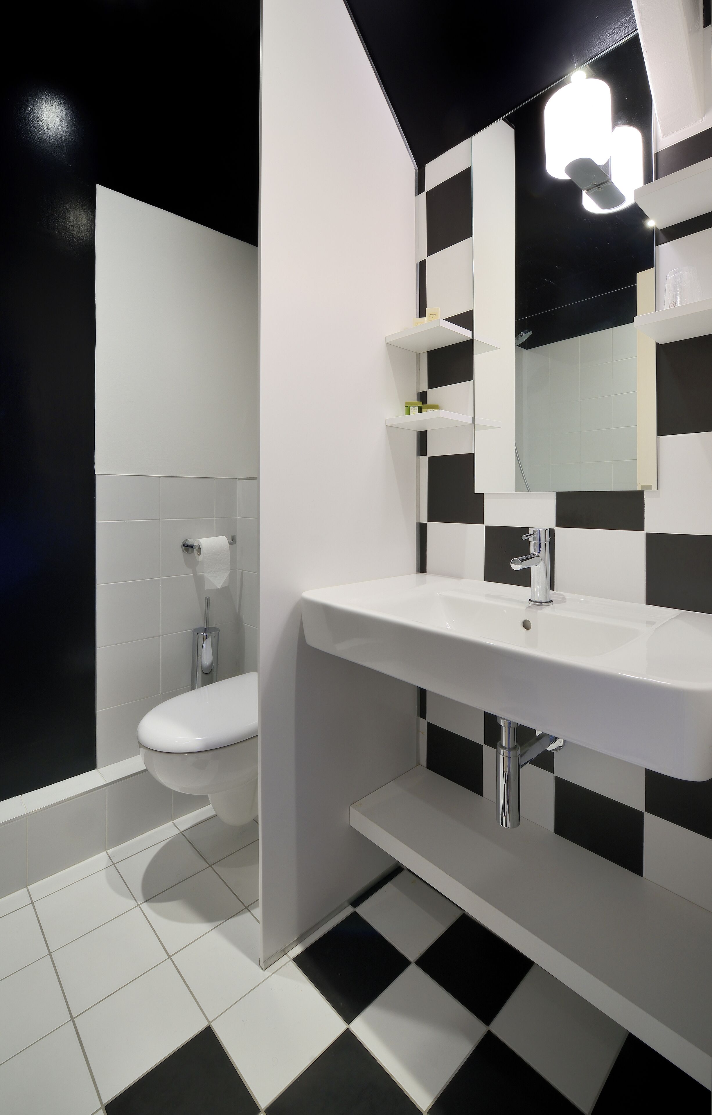 A modern bathroom with a white sink, black and white checkered floor, and a toilet with a roll of toilet paper.