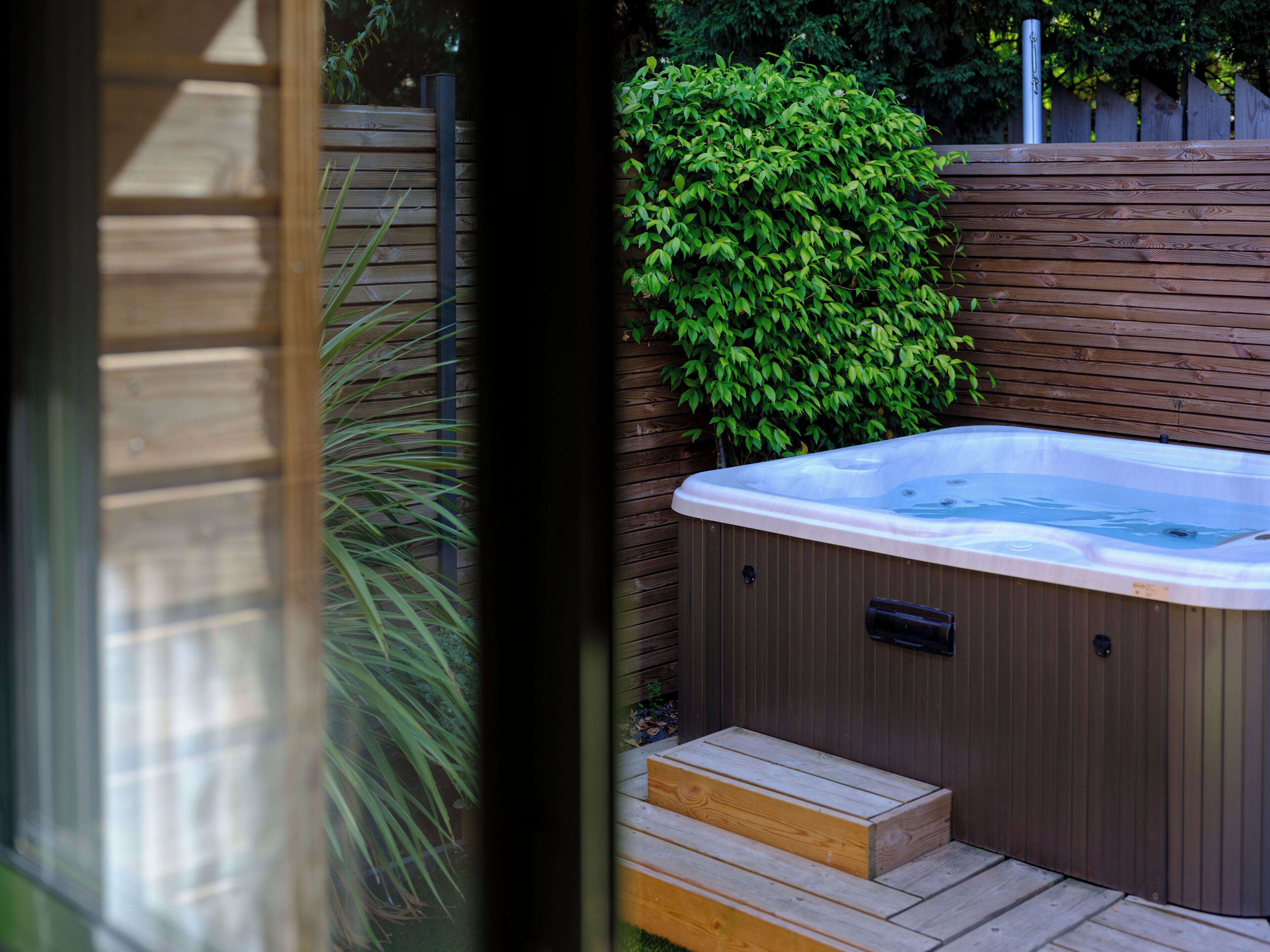 A hot tub with wooden steps leading up to it, surrounded by a wooden fence and greenery.