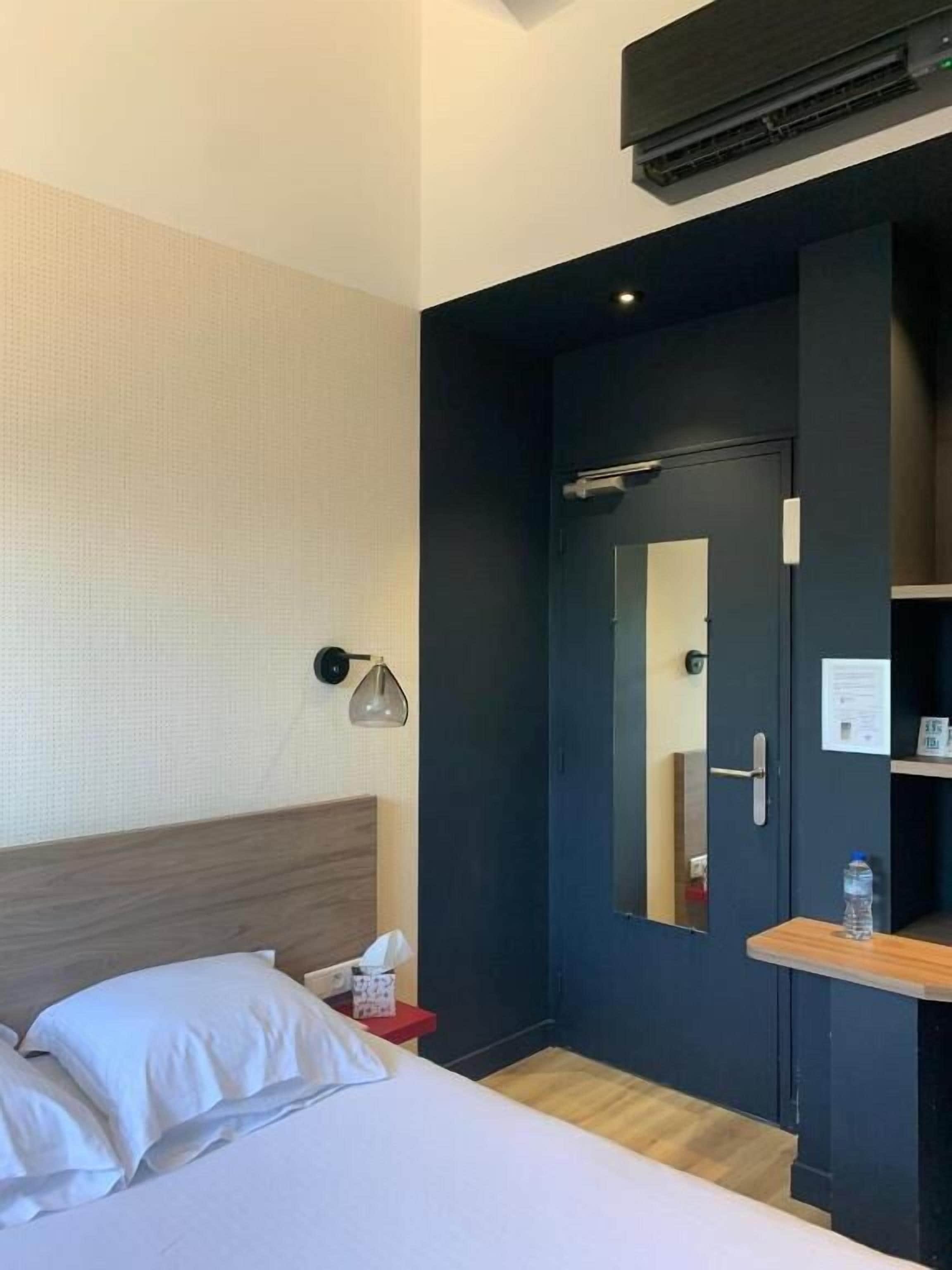 Quarto de hotel com cama, mesa de cabeceira, abajur e espelho.