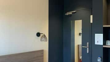 Quarto de hotel com cama, mesa de cabeceira, abajur e espelho.