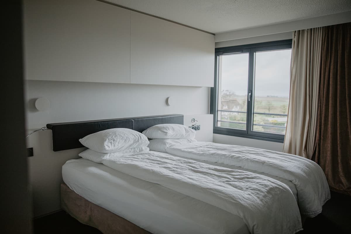 Ett hotellrum med en stor säng, ett fönster med gardiner och utsikt över omgivningarna.