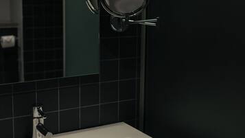 Een badkamer met een wit wastafel, een spiegel en donkere betegelde wanden.