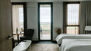 Camera d'albergo con un letto, una scrivania, una sedia, un tavolino e vista all'esterno attraverso una porta.