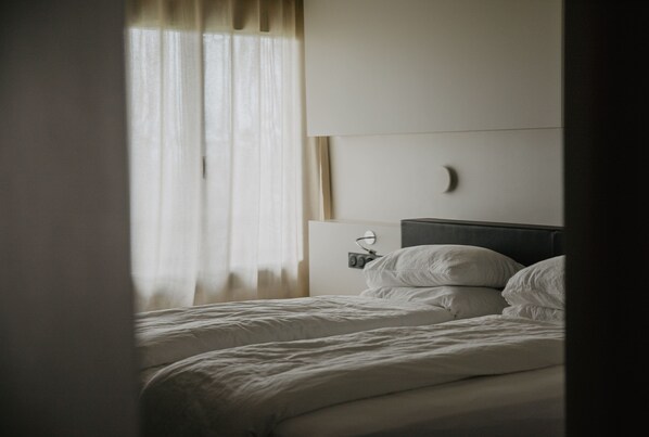 Una habitación de hotel con cama, mesita de noche y ventana con cortinas.