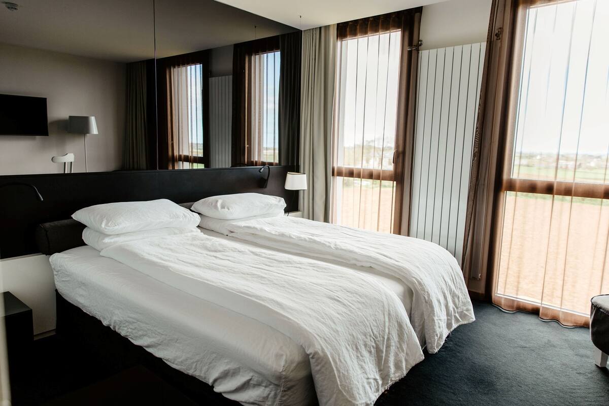 Ett hotellrum med en stor säng, en platt-TV som är monterad på väggen och utsikt över omgivningarna genom fönstret.