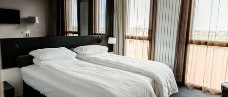 A hotel room with a large bed, a flat-screen TV mounted on the wall, and a view of the outdoors through the window.