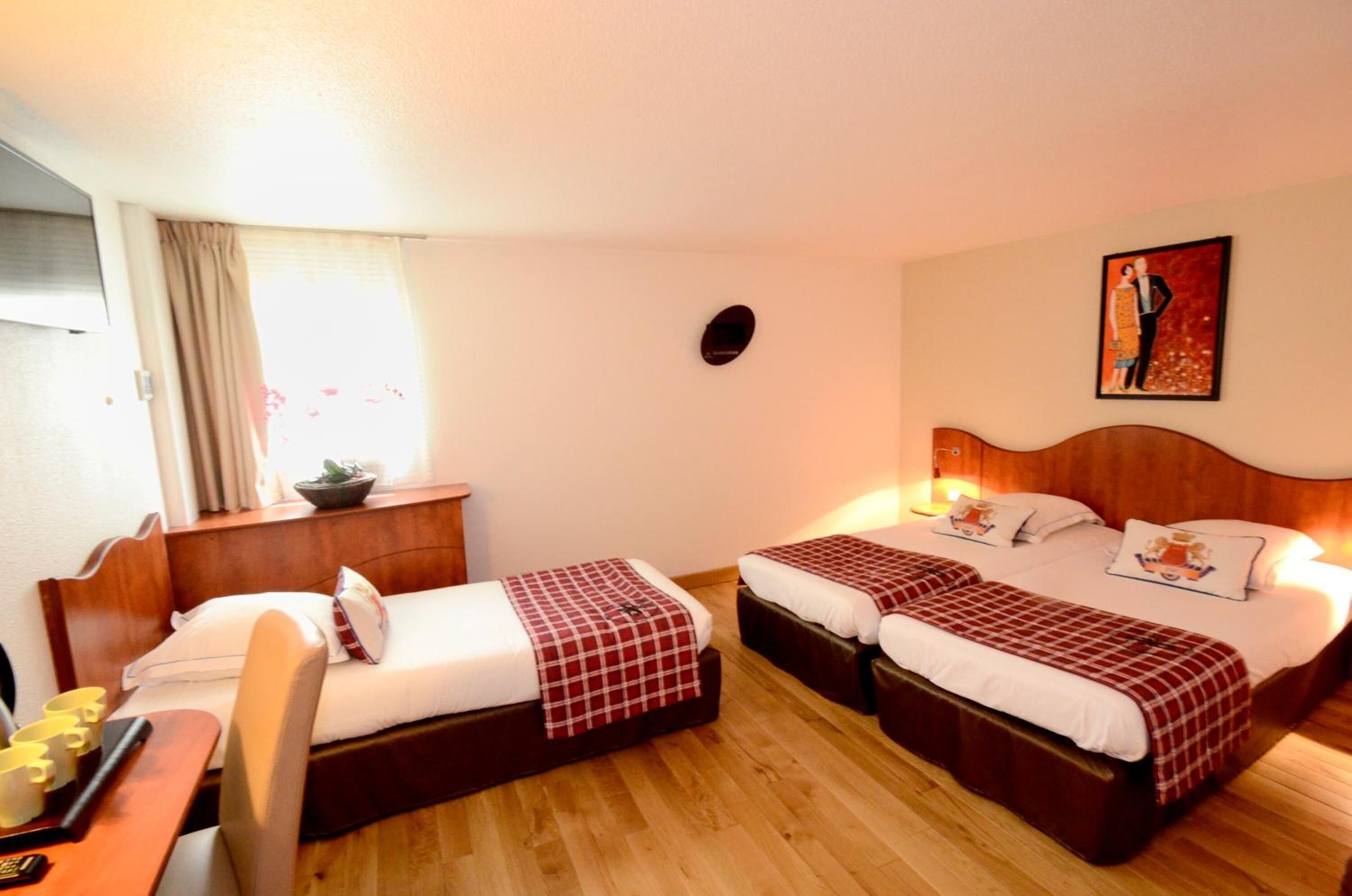 A hotel room with two beds, a desk, a chair, a window with curtains, and a painting on the wall.