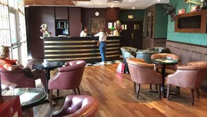 A restaurant interior with wooden flooring, leather chairs, a counter with staff, and a green wall with a mounted animal head. - Green hôtels  Parc des Expositions (Tremblay-en-France)