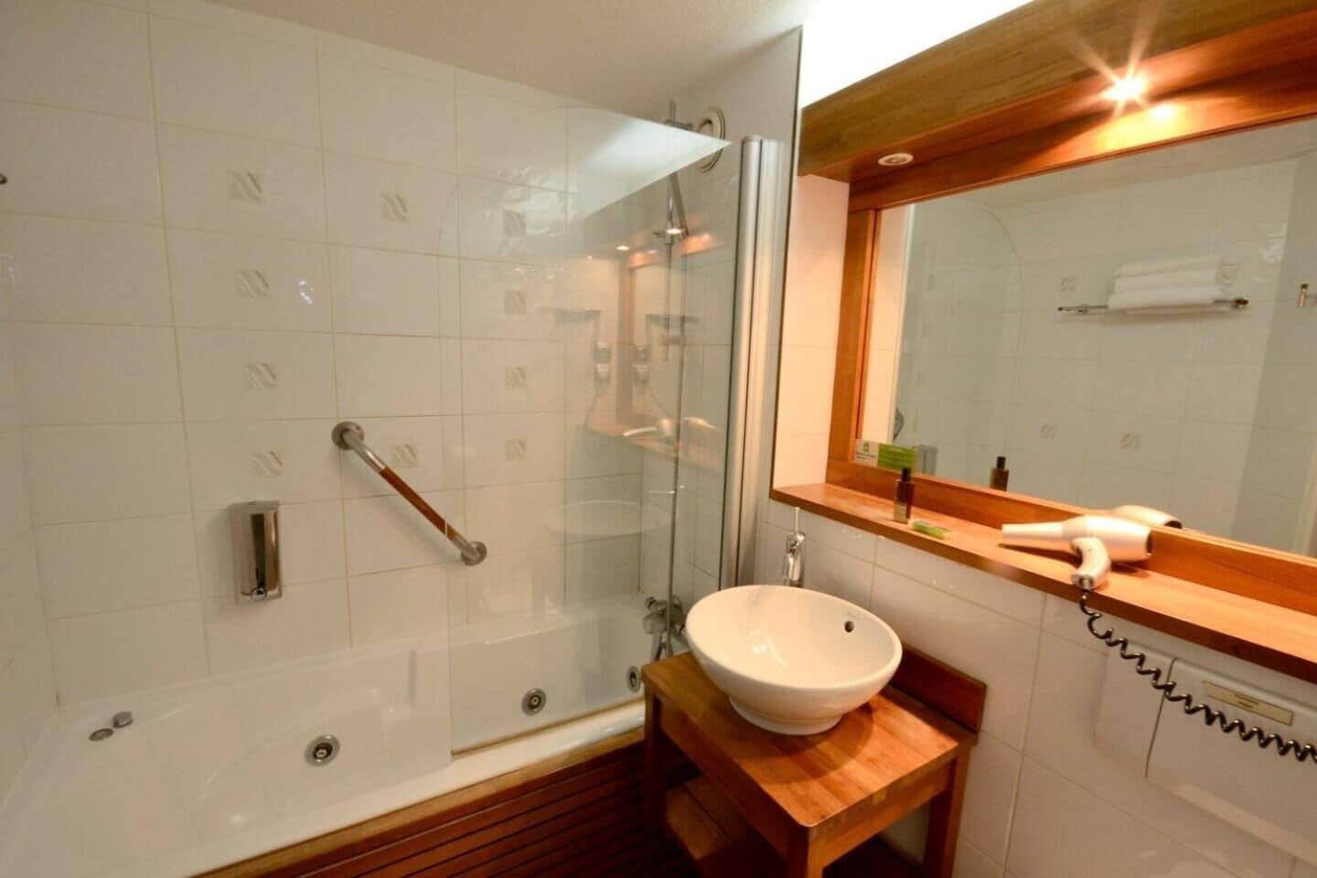 A bathroom with a glass-enclosed shower, a wooden vanity, a white sink, and a mirror with a wooden frame.