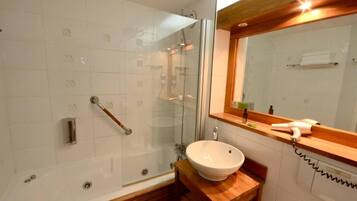 A bathroom with a glass-enclosed shower, a wooden vanity, a white sink, and a mirror with a wooden frame.