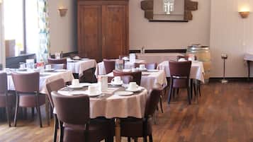 A dining area with tables set for service, wooden flooring, and a large wooden cabinet in the background.