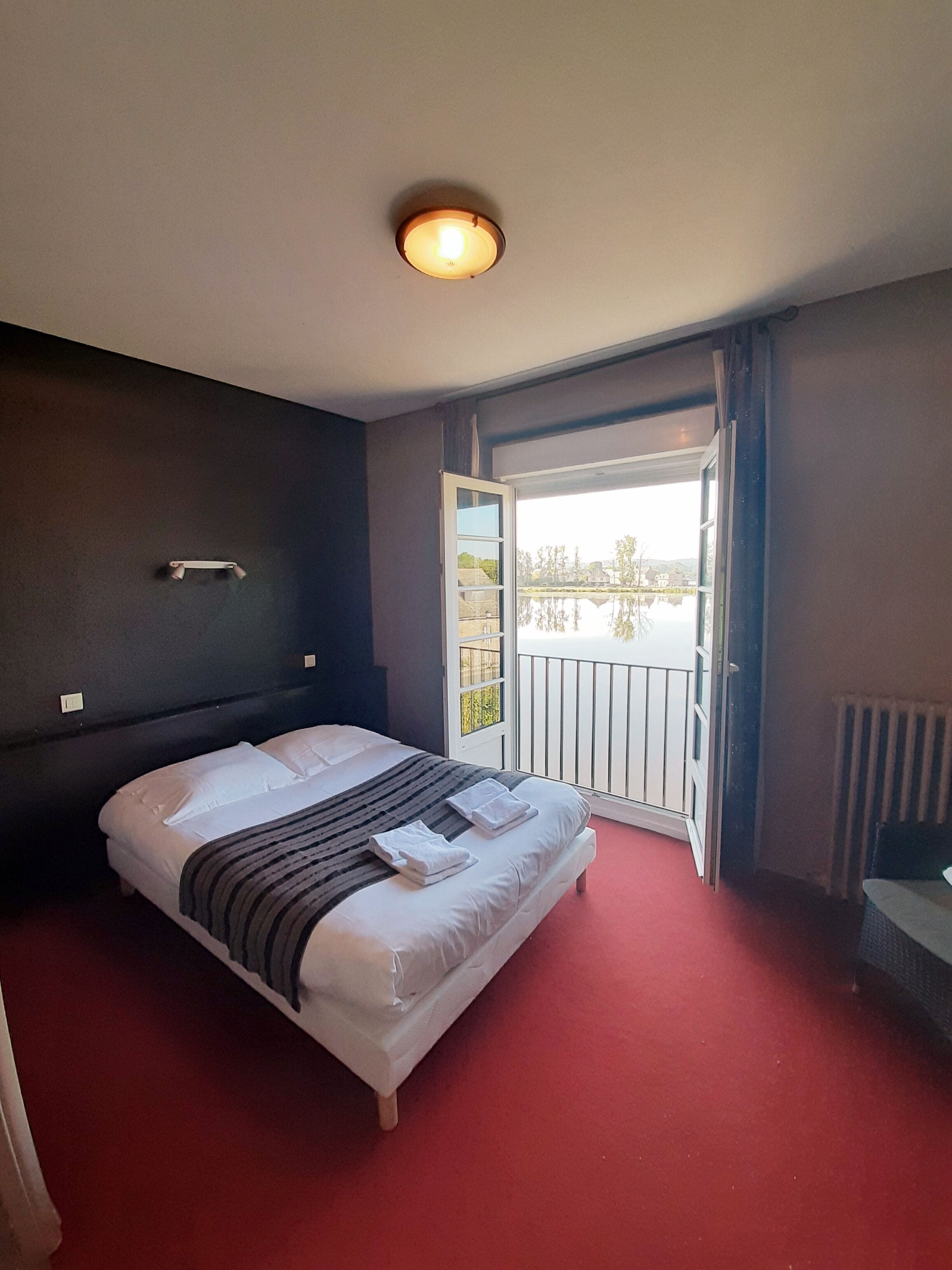 Una habitación de hotel con cama, ventana con vistas, puerta y una lámpara en el techo.