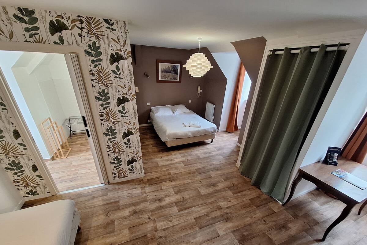 A bedroom with a bed, wooden flooring, a desk, and a green curtain.