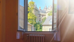 Een hotelkamer met twee bedden, een raam met uitzicht op een kasteel en een radiator.
