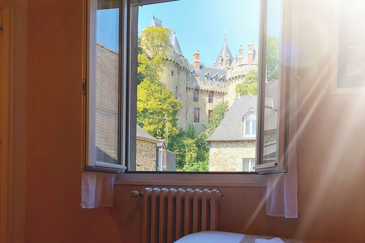 A hotel room with two beds, a window with a view of a castle, and a radiator.