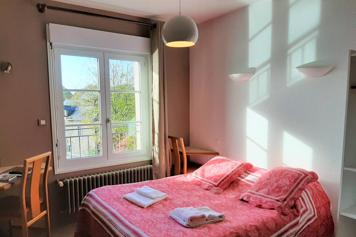 A bedroom with a large bed, a window, a desk, and a chair.