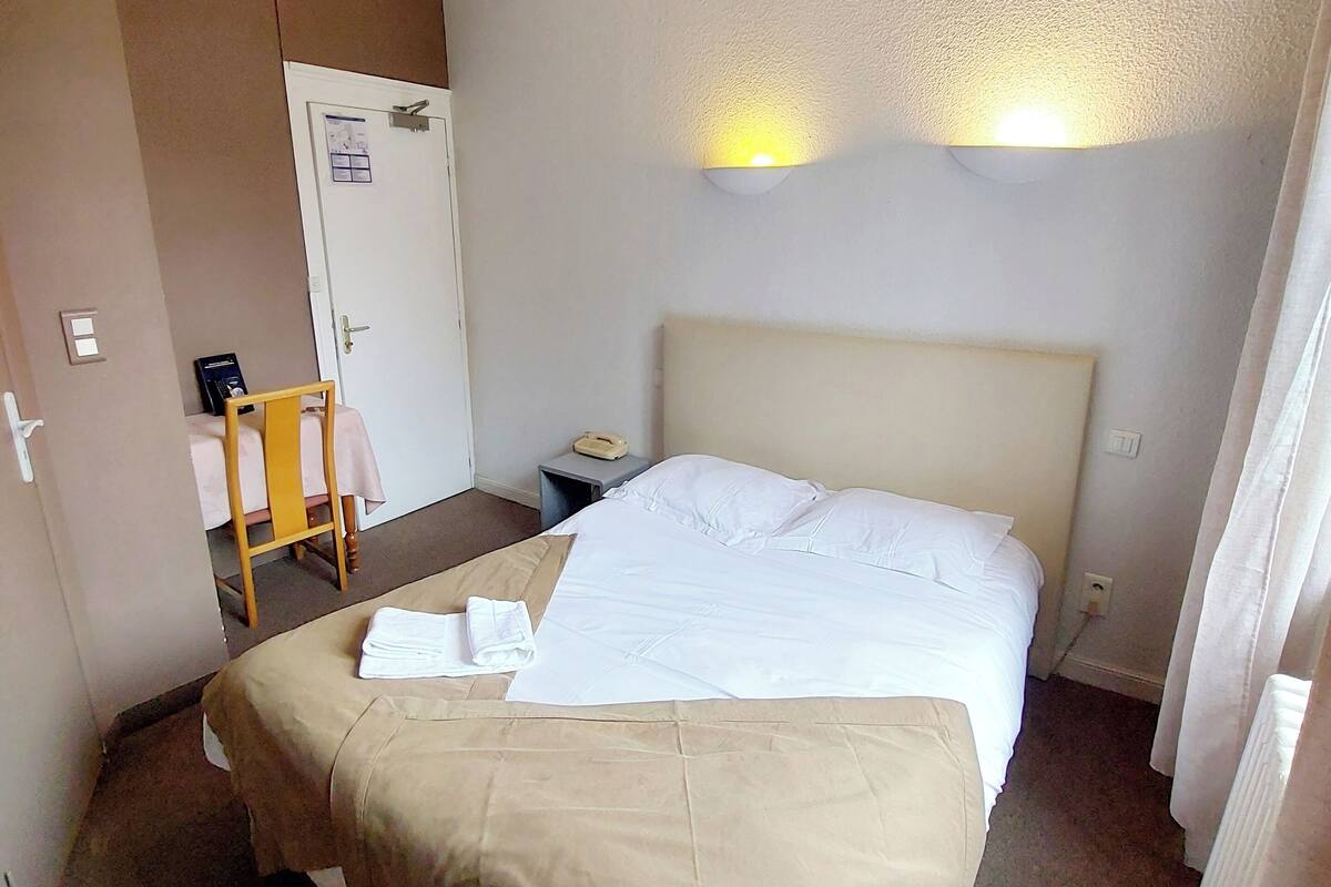 A hotel room with a large bed, a bedside table, a chair, and a door with a calendar.