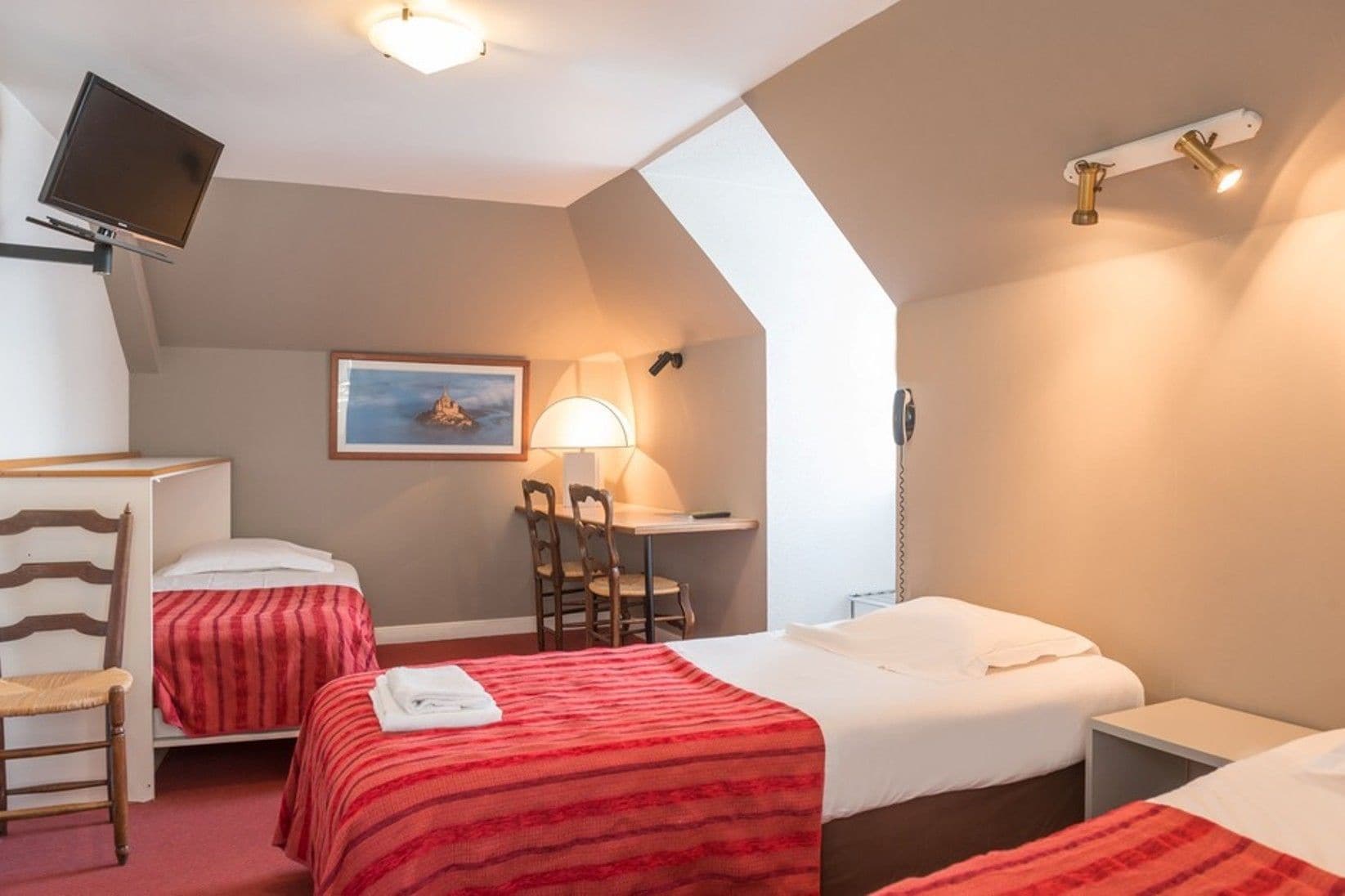 A hotel room with two beds, a desk, a chair, a television, and a lamp.