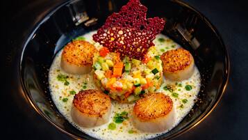 A dish with scallops, a vegetable medley, and a decorative element on a plate.