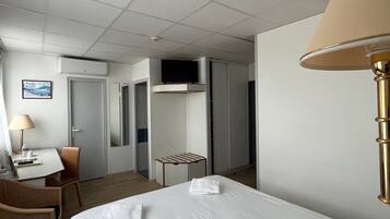 A hotel room with a bed, a desk with a chair, a television, and a lamp.