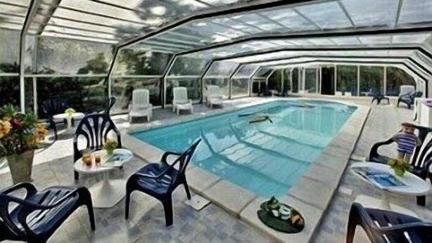 A covered outdoor swimming pool with lounge chairs and tables, surrounded by a glass enclosure. - Hôtel de la Mer (La Tranche-sur-Mer)