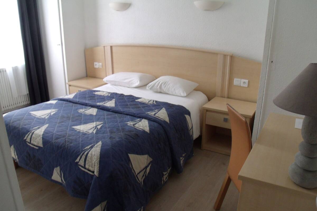 A hotel room with a bed, a desk, and a lamp.