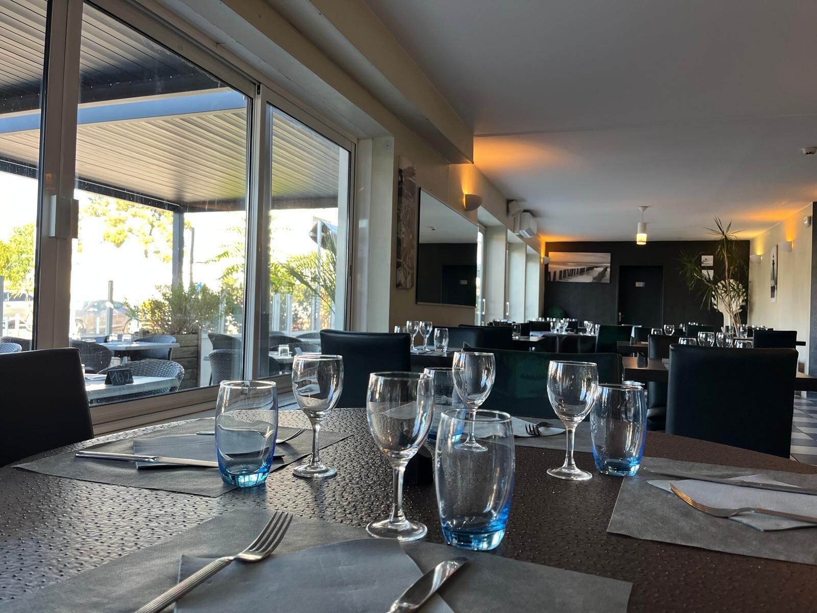 Un espace repas avec des tables dressées pour le repas, de grandes fenêtres et une vue sur l’extérieur.