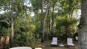 A garden with a round table and a bench, surrounded by trees and plants. - Hôtel de la Mer (La Tranche-sur-Mer)
