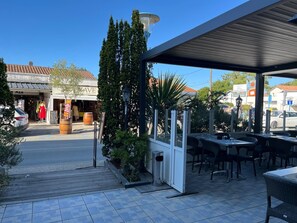 An outdoor cafe with tables and chairs, a covered seating area, and a storefront with a sign. - Hôtel de la Mer (La Tranche-sur-Mer)