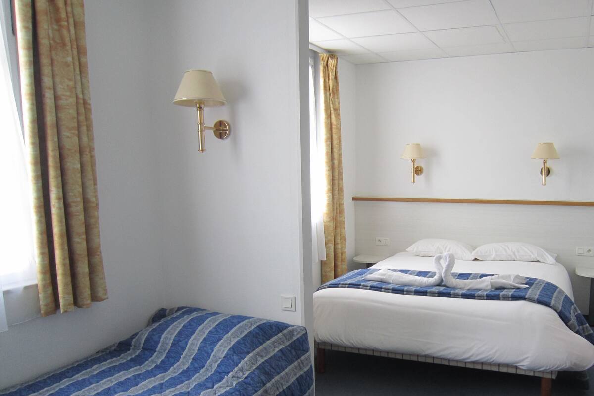 A hotel room with two beds, a window with curtains, wall-mounted lamps, and a headboard.