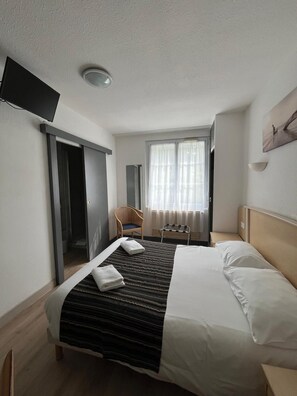 A hotel room with a bed, a chair, a television, and a window with curtains.