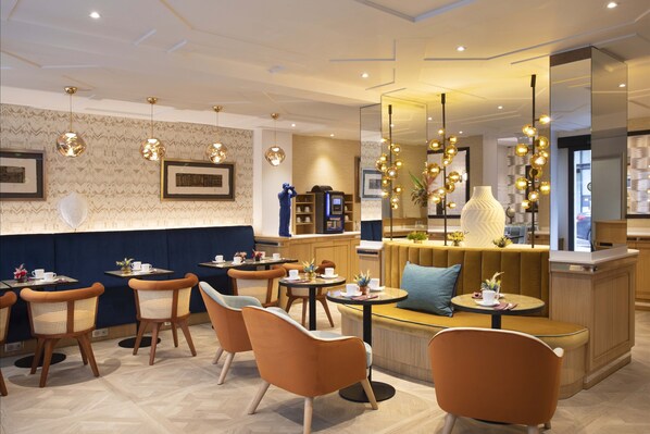 A modern restaurant with round tables, orange chairs, and a bar area. - Hôtel Phileas Lazare & Spa - Opéra (Paris)